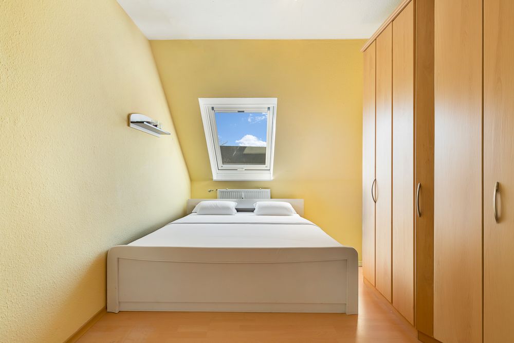 Helles Schlafzimmer mit Doppelbett, Dachfenster und großem Holzkleiderschrank.