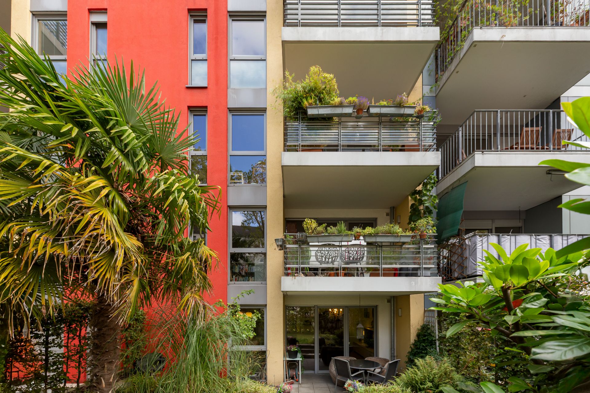 Moderne Wohnhausfassade mit Balkonen und viel Grün im Vordergrund.