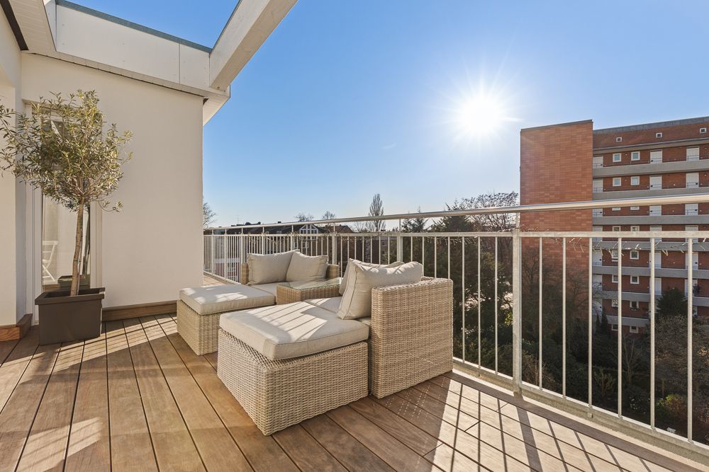 Moderne Terrasse mit Holzboden, Sitzmöbeln, Pflanze und Geländer bei Sonnenschein.
