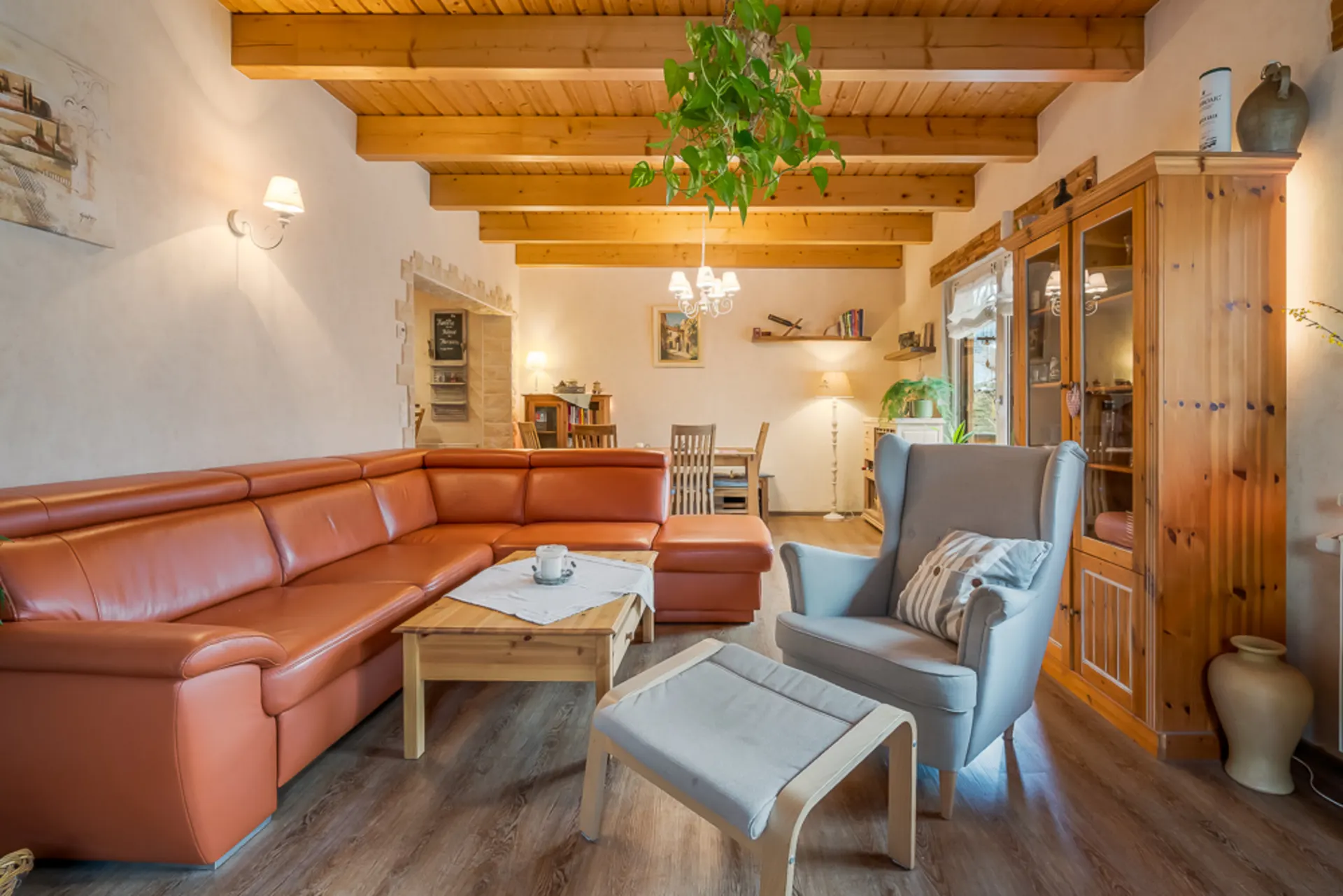 Wohnzimmer mit orangefarbener Eckcouch, Sessel, Couchtisch und Holzmöbeln, sichtbare Holzbalkendecke.