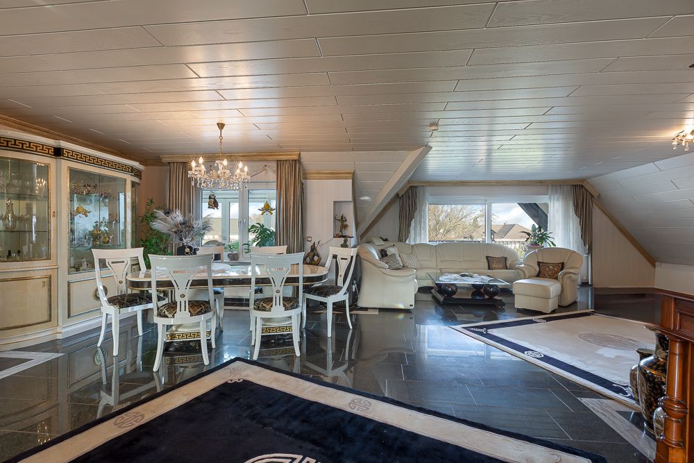 Helles Wohnzimmer mit Esstisch, Stühlen, Sofa, Teppichen und großen Fenstern.