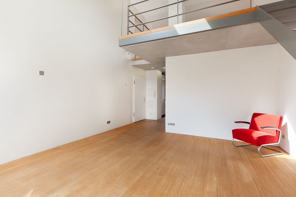 Helles Wohnzimmer mit Holzfußboden, rotem Sessel und Galerieebene oben.