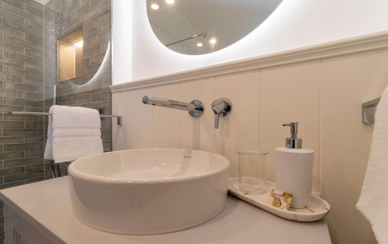 Modernes Badezimmer mit rundem Waschbecken, Spiegel, Handtüchern und Seifenspender.