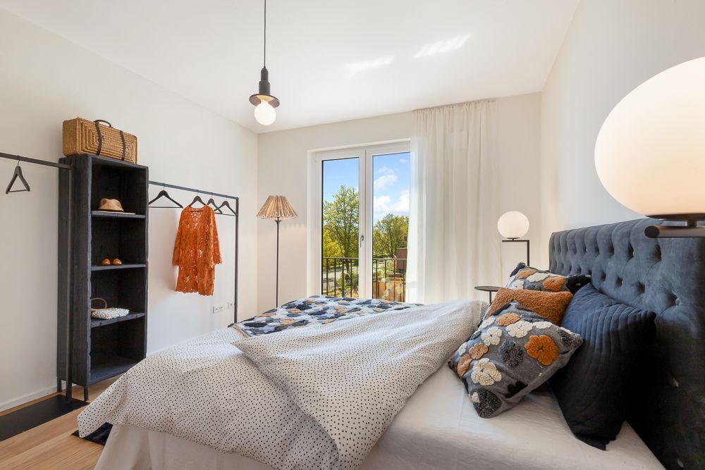 Helles Schlafzimmer mit Doppelbett, offenem Kleiderschrank und Fenstertür mit Blick ins Grüne.