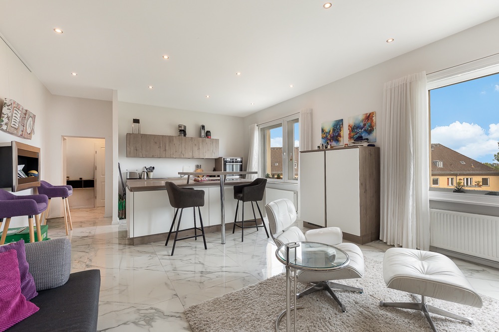 Helles Wohnzimmer mit offener Küche, modernen Möbeln und großen Fenstern.