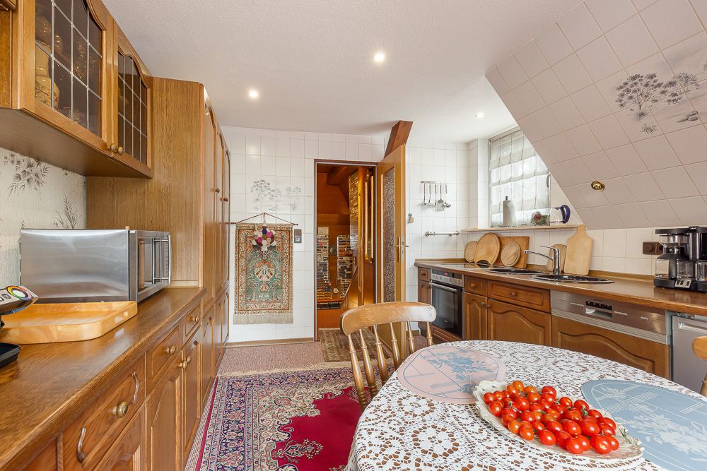 Küche mit Holzmöbeln, Esstisch mit Tischdecke und Schale voller Tomaten, Teppich auf dem Boden.