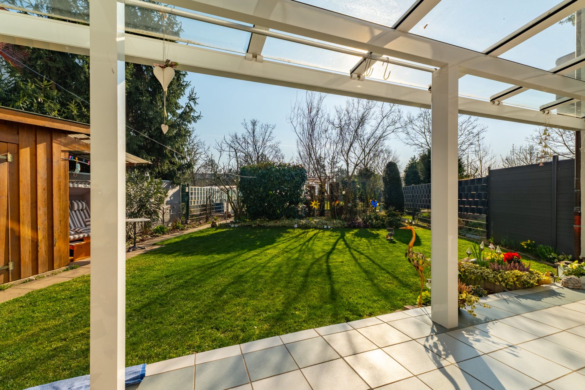 Überdachte Terrasse mit Blick auf grünen Garten und Holzschuppen.