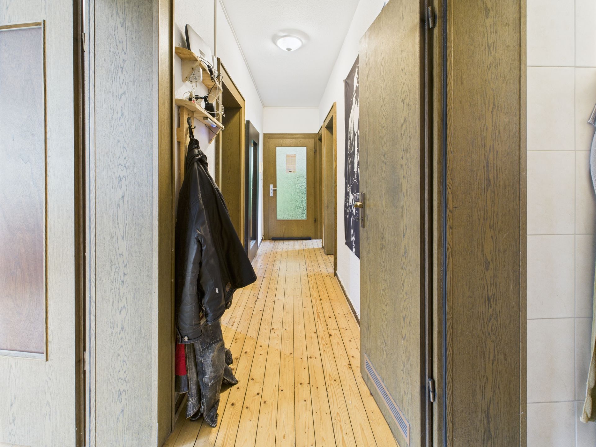 Langer Flur mit Holzboden, mehreren Türen und einer Garderobe mit Jacken an der Wand.