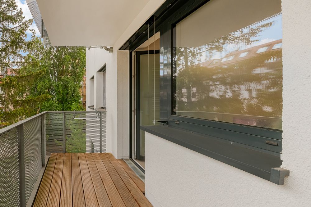 Moderner Balkon mit Holzboden und Metallgeländer an einem Wohngebäude, große Fenster zur Seite.