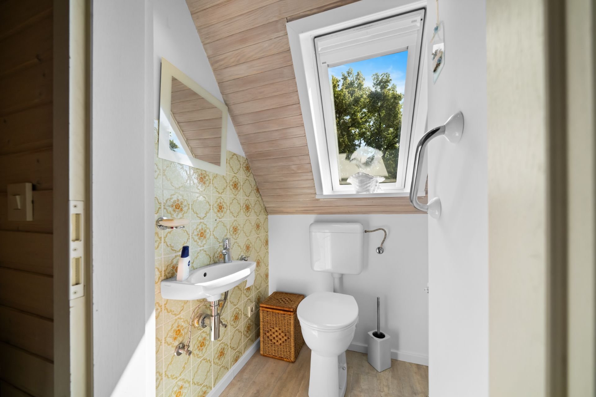 Kleines Badezimmer mit Toilette, Waschbecken, Spiegel und Dachfenster.