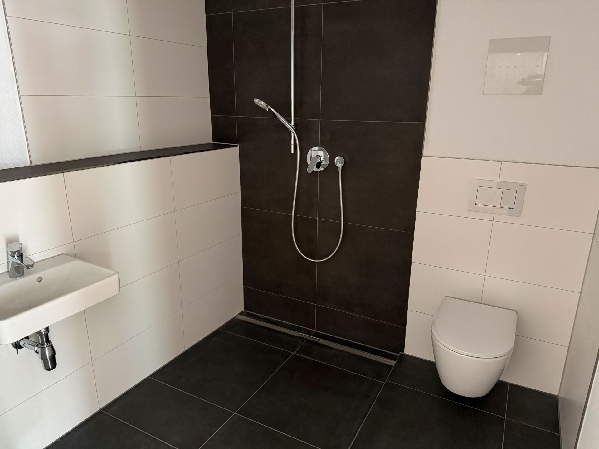 Modernes Badezimmer mit bodengleicher Dusche, Waschbecken und Wandtoilette.