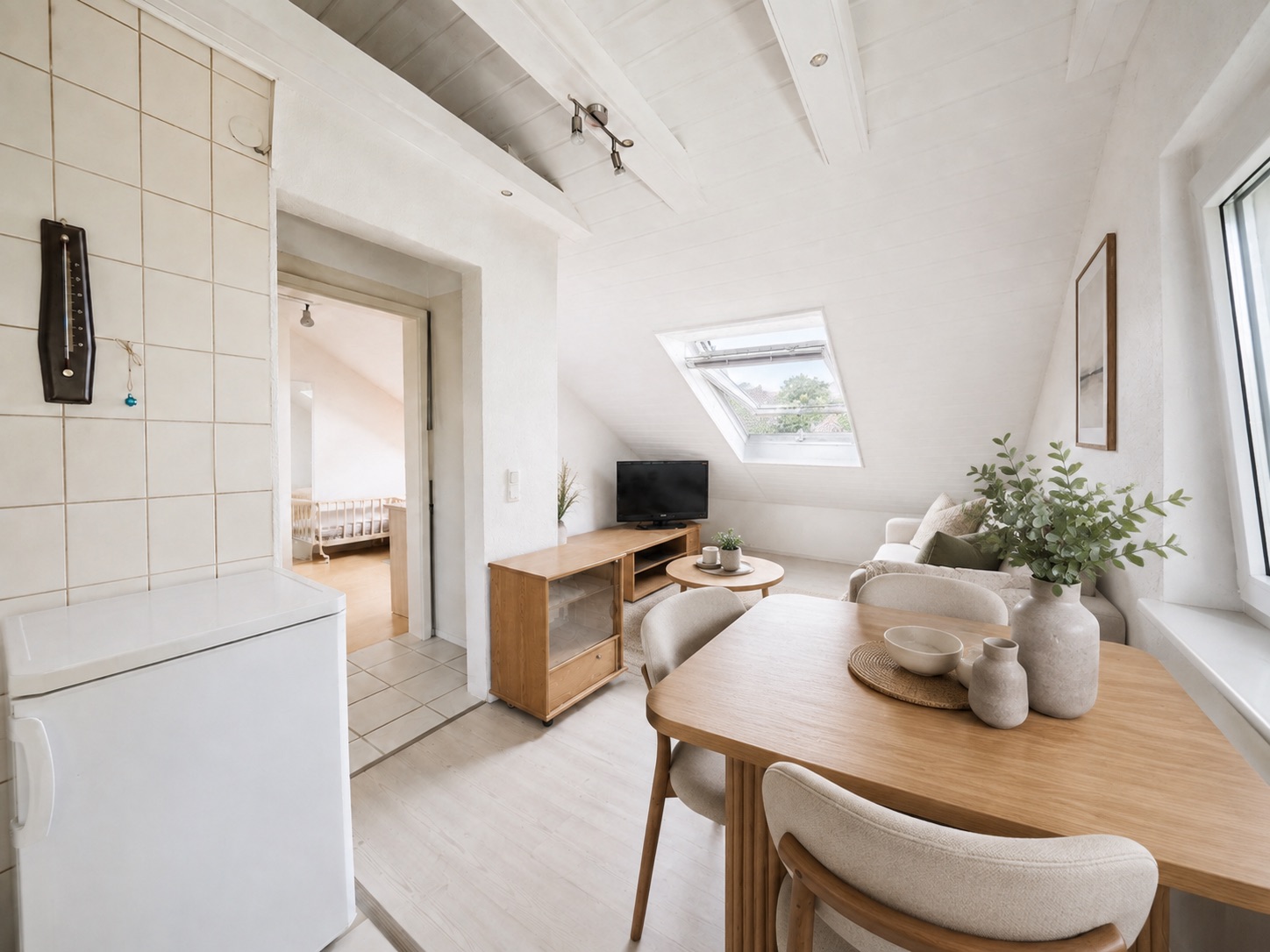Helles Wohnzimmer mit Esstisch, Sofa, Fernseher und großem Fenster in einer Dachwohnung.