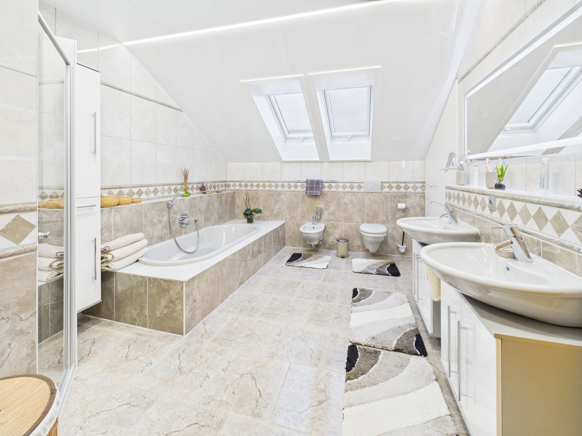 Helles Badezimmer mit Badewanne, zwei Waschbecken, WC, Bidet und Dachfenstern.