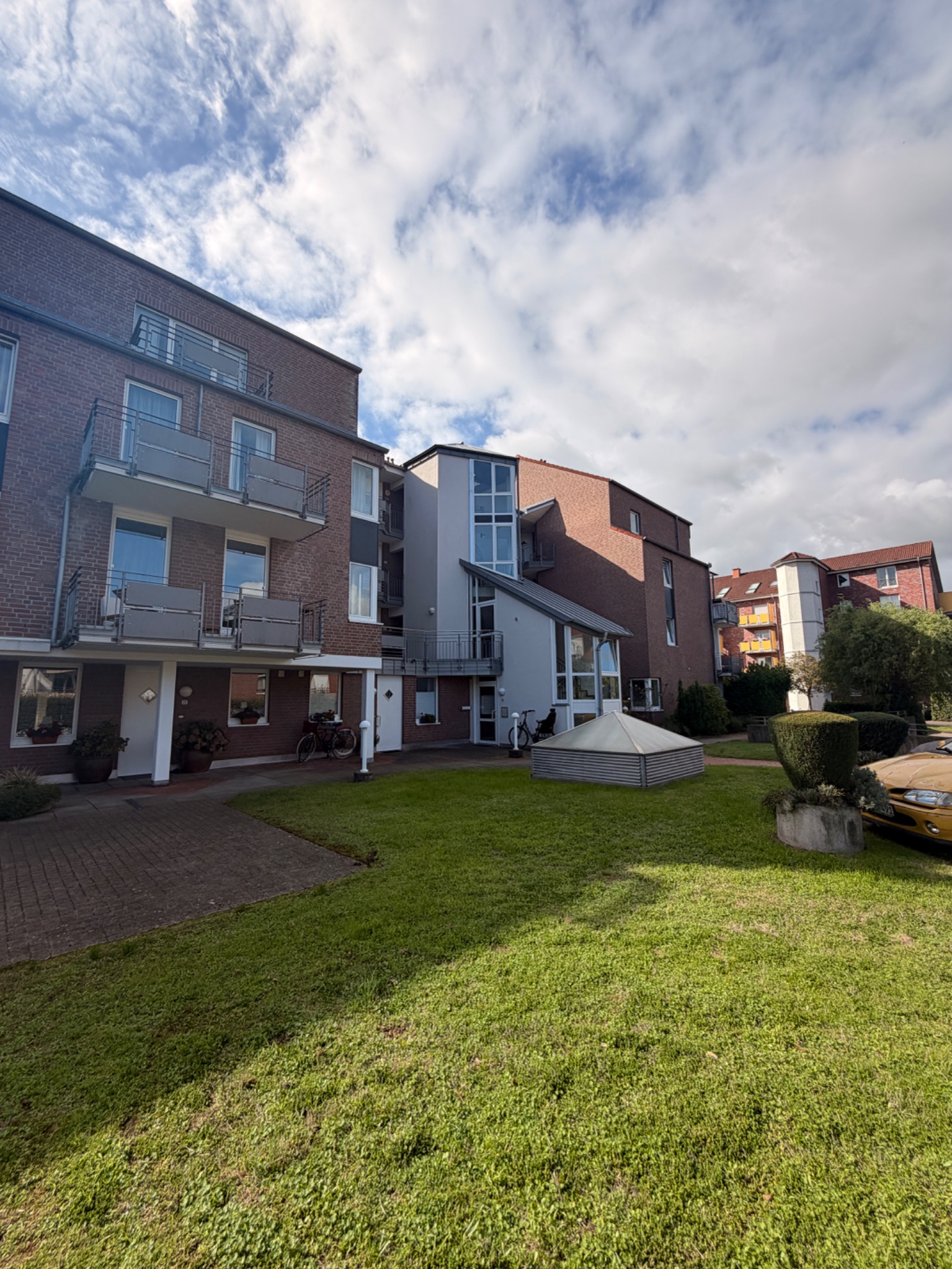 Mehrfamilienhaus mit Balkonen, Vorgarten und kleinem Parkplatz im Vordergrund.