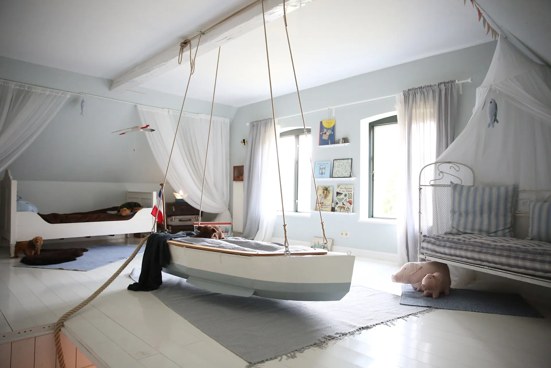Helles Kinderzimmer mit Schaukelbett in Bootform, zwei Betten und Spielzeugen.
