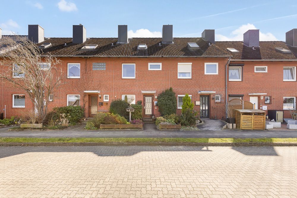 Reihenhaus mit rotem Backstein, Vorgärten und mehreren Eingängen, Straße im Vordergrund.
