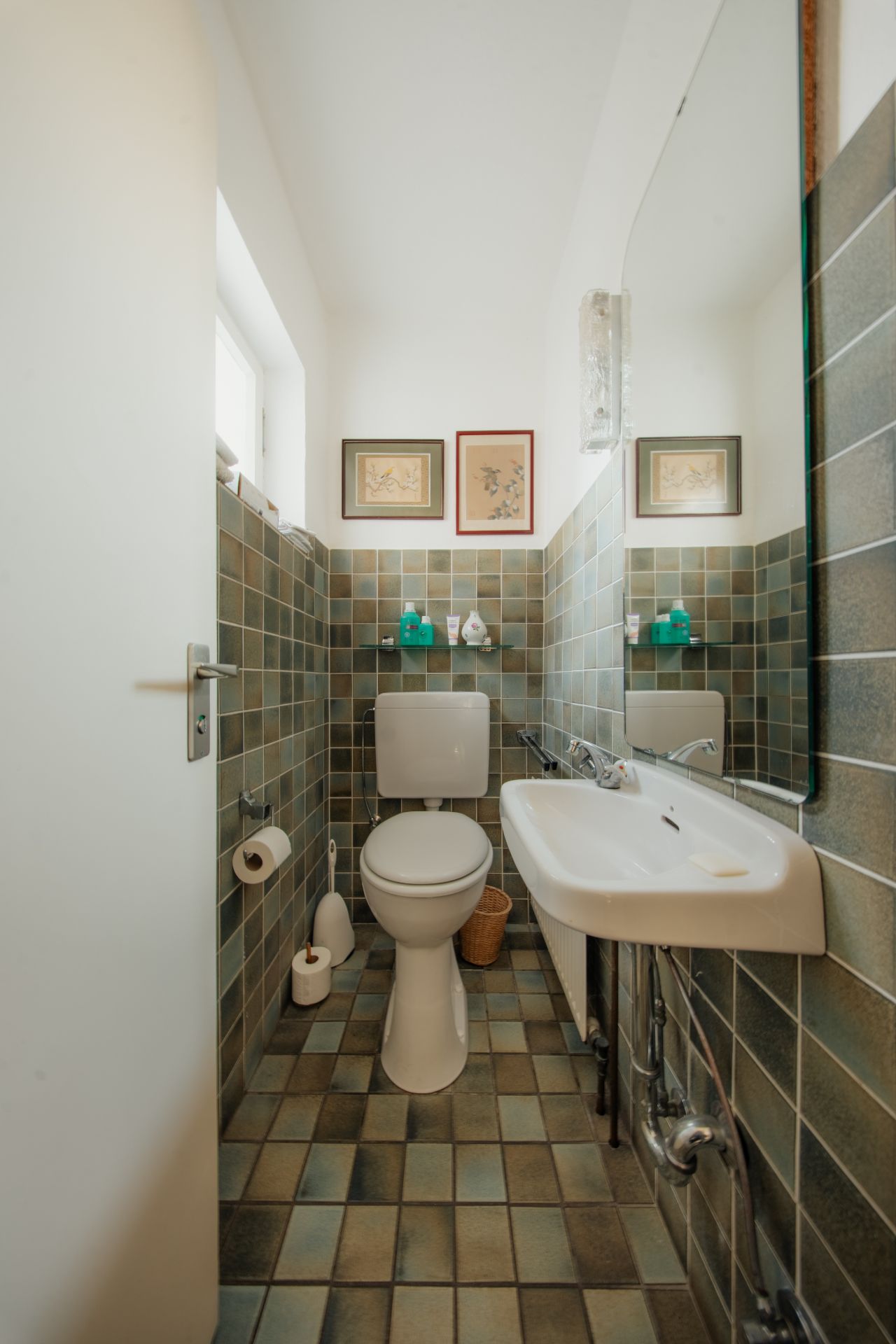 Kleines Badezimmer mit Toilette, Waschbecken, gefliesten Wänden und drei Bildern an der Wand.