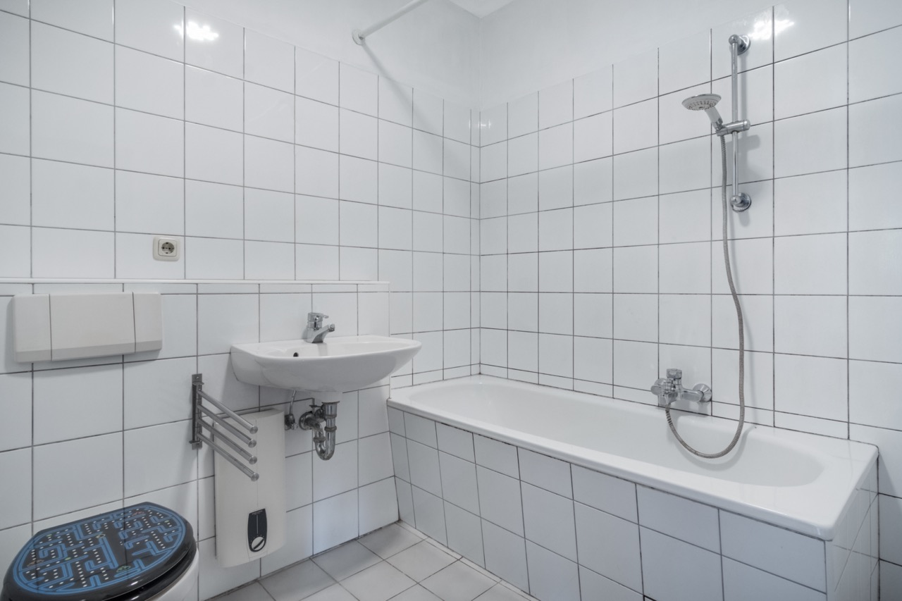 Weiß gefliestes Badezimmer mit Badewanne, Duschkopf, Waschbecken und Toilette.
