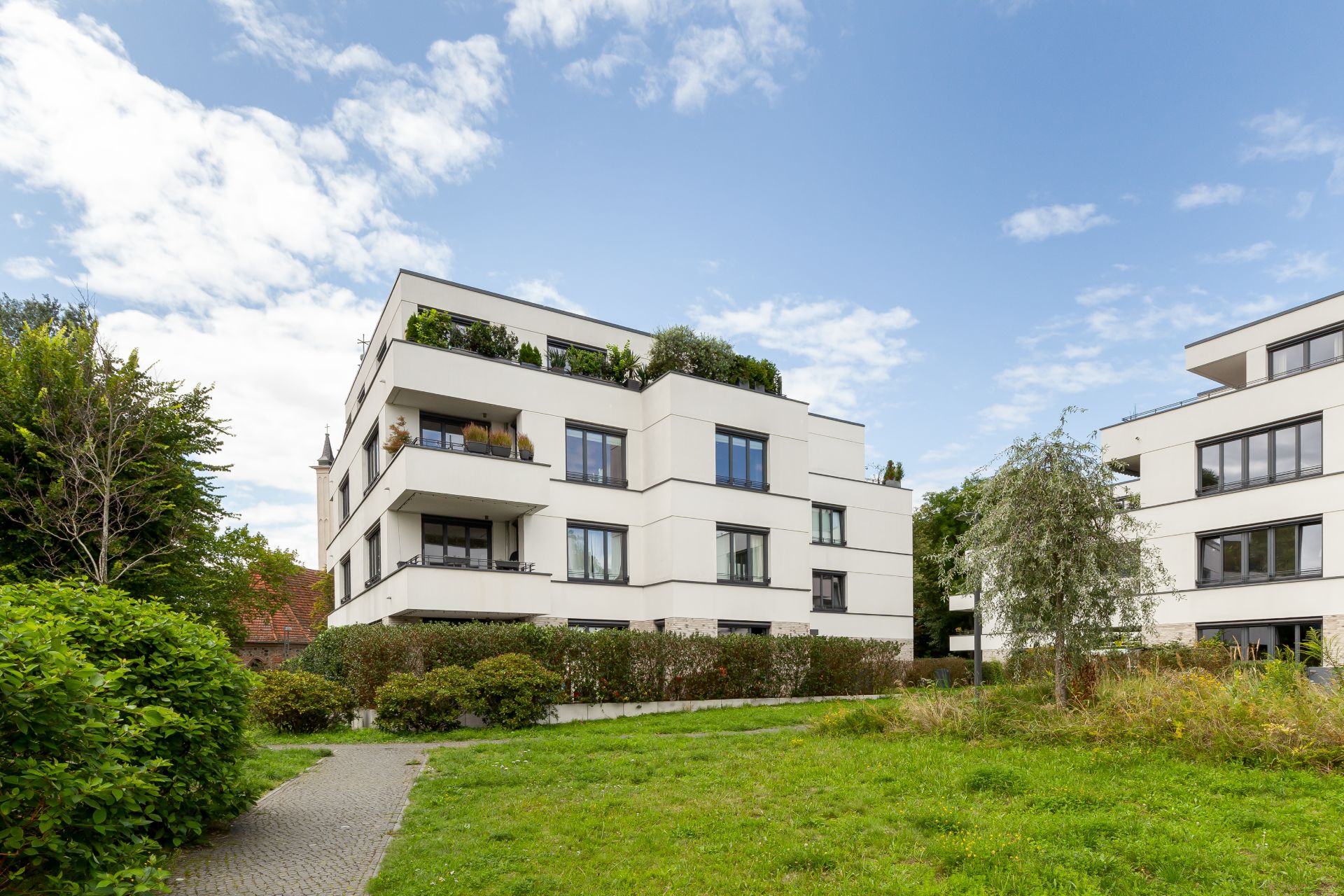 Modernes weißes Wohngebäude mit mehreren Balkonen und umliegender Grünfläche.