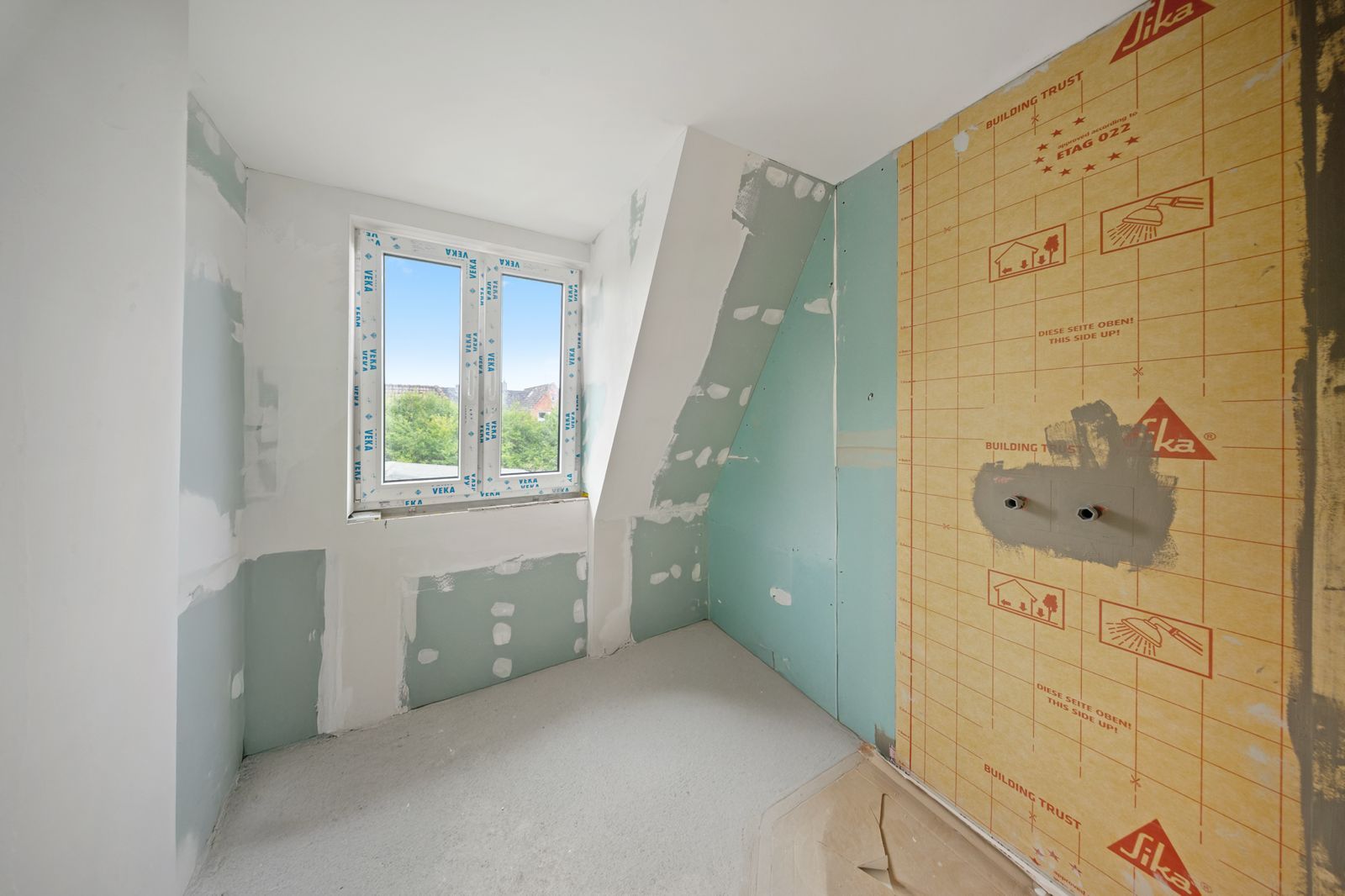 Kleiner Raum im Rohbau mit Fenster, Rigipswänden und unfertigem Boden.
