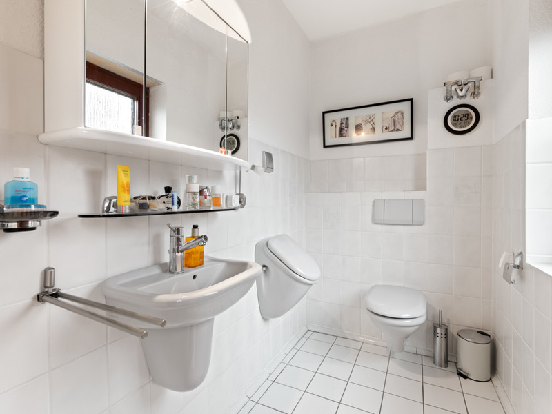 Helles Badezimmer mit Waschbecken, Urinal, Toilette, Spiegel und weißen Fliesen.