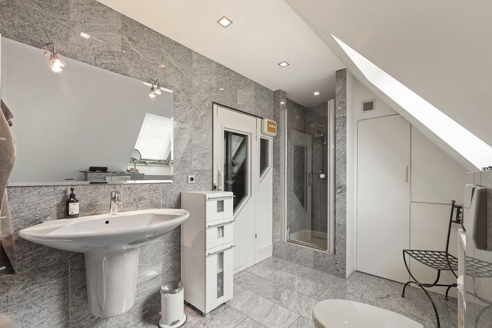 Modernes Badezimmer mit grauen Fliesen, Waschbecken, Spiegel, Dusche und Fenster.