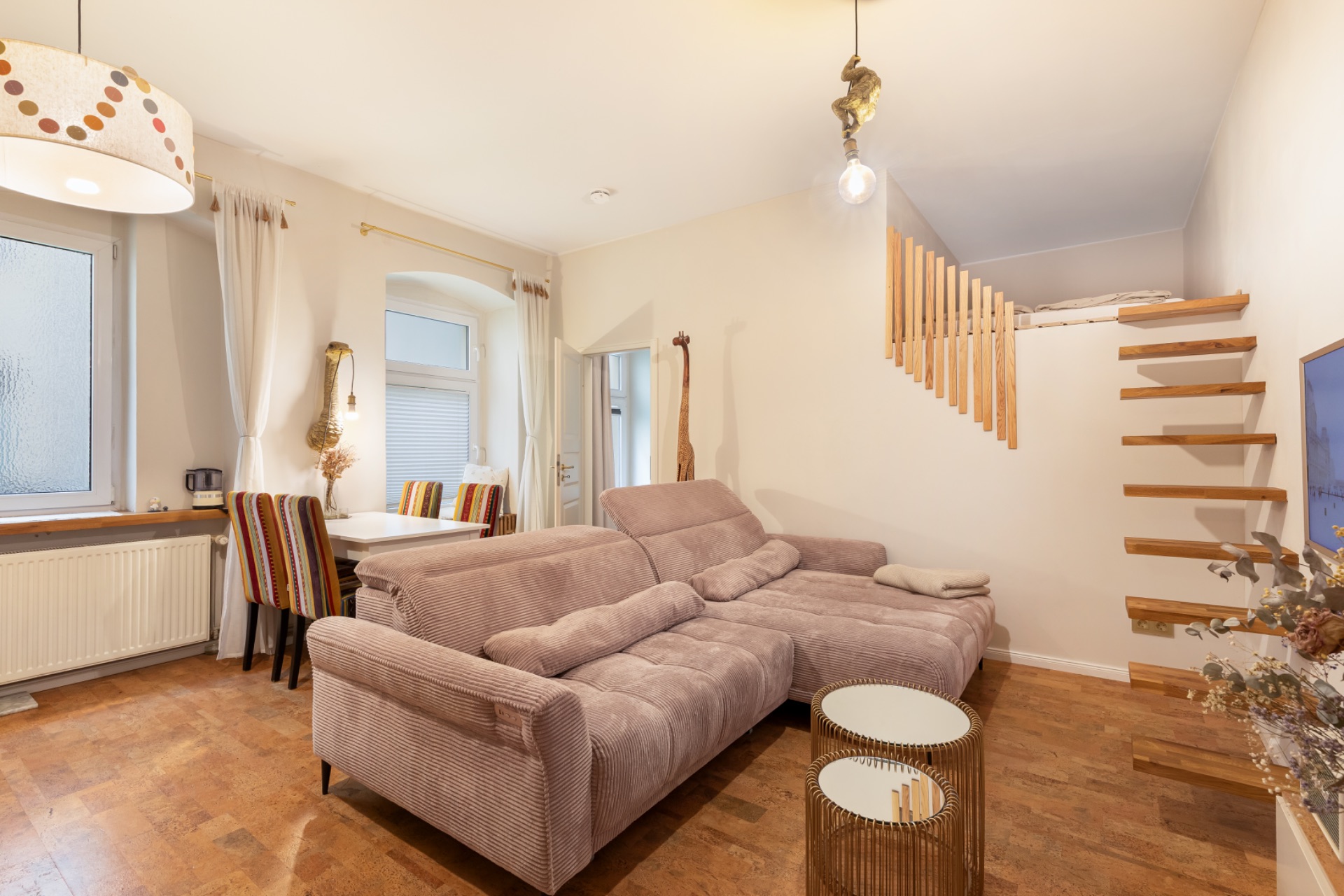 Helles Wohnzimmer mit Sofa, zwei runden Tischen und offener Holztreppe zum Hochbett.