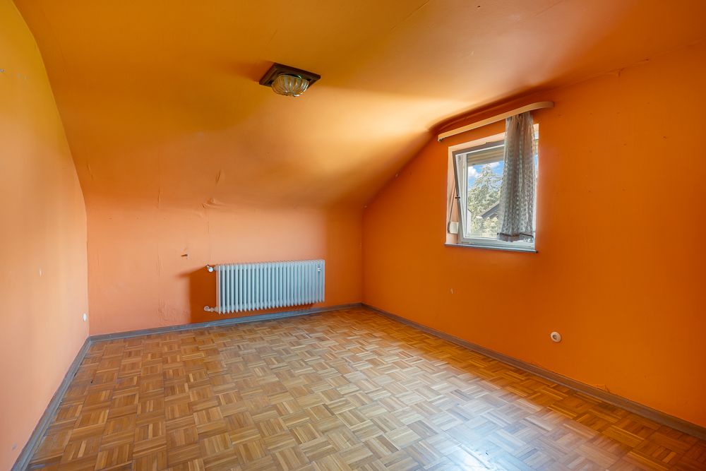 Leerer Raum mit orangefarbenen Wänden, Holzboden, Heizkörper und Fenster mit Vorhang.