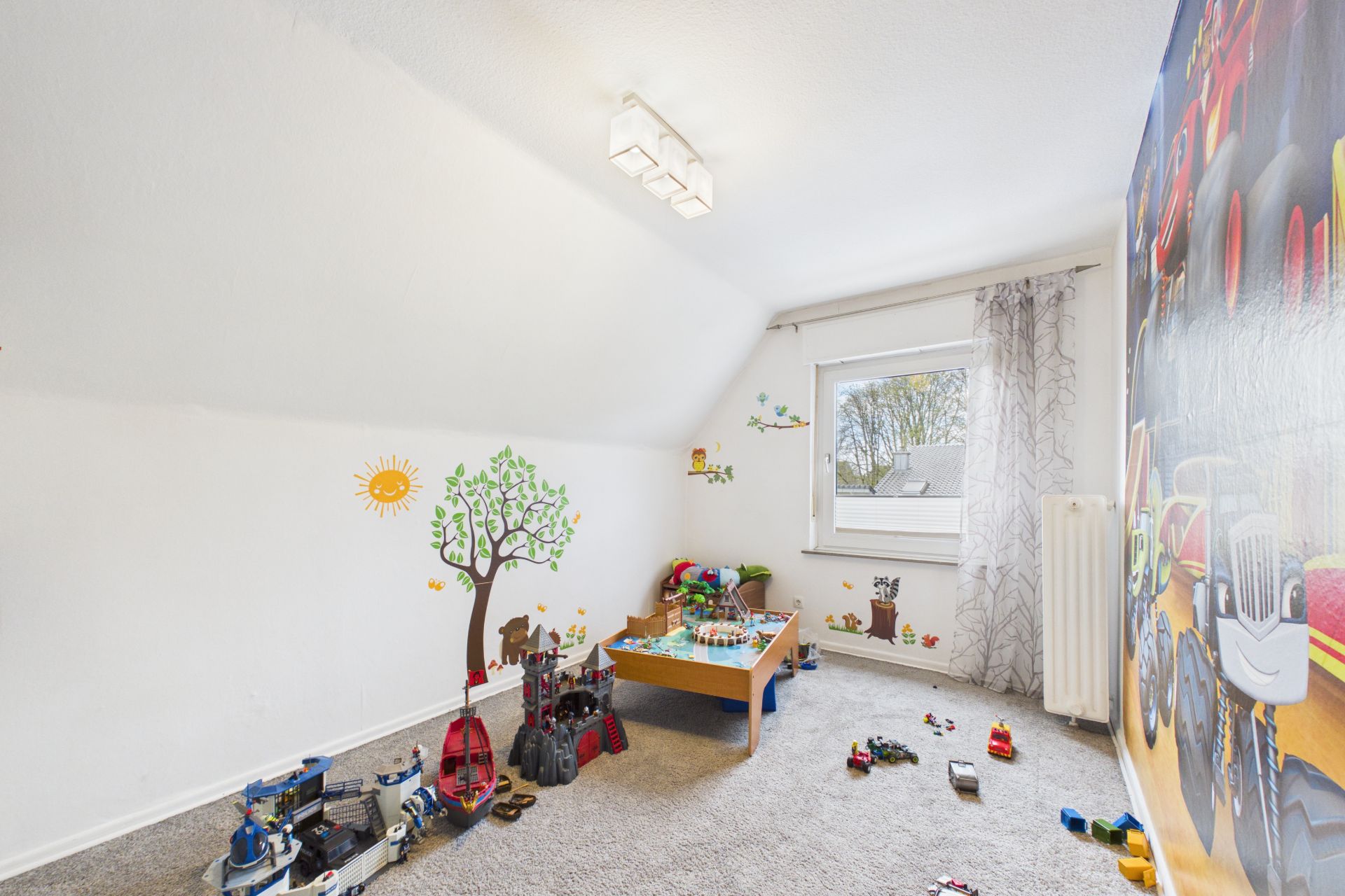 Helles Kinderzimmer mit Spielzeug, Wandtattoos und Teppichboden.