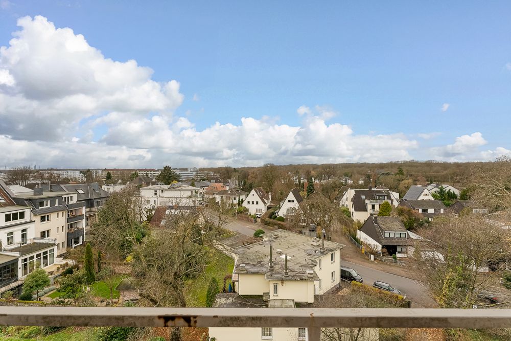 Blick von oben auf ein Wohnviertel mit Häusern, Bäumen und einer Straße an einem bewölkten Tag.