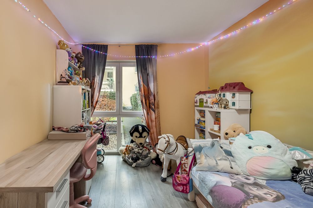 Kinderzimmer mit Spielzeug, kleinem Bett, Schreibtisch, Regalen und Lichterkette an der Decke.