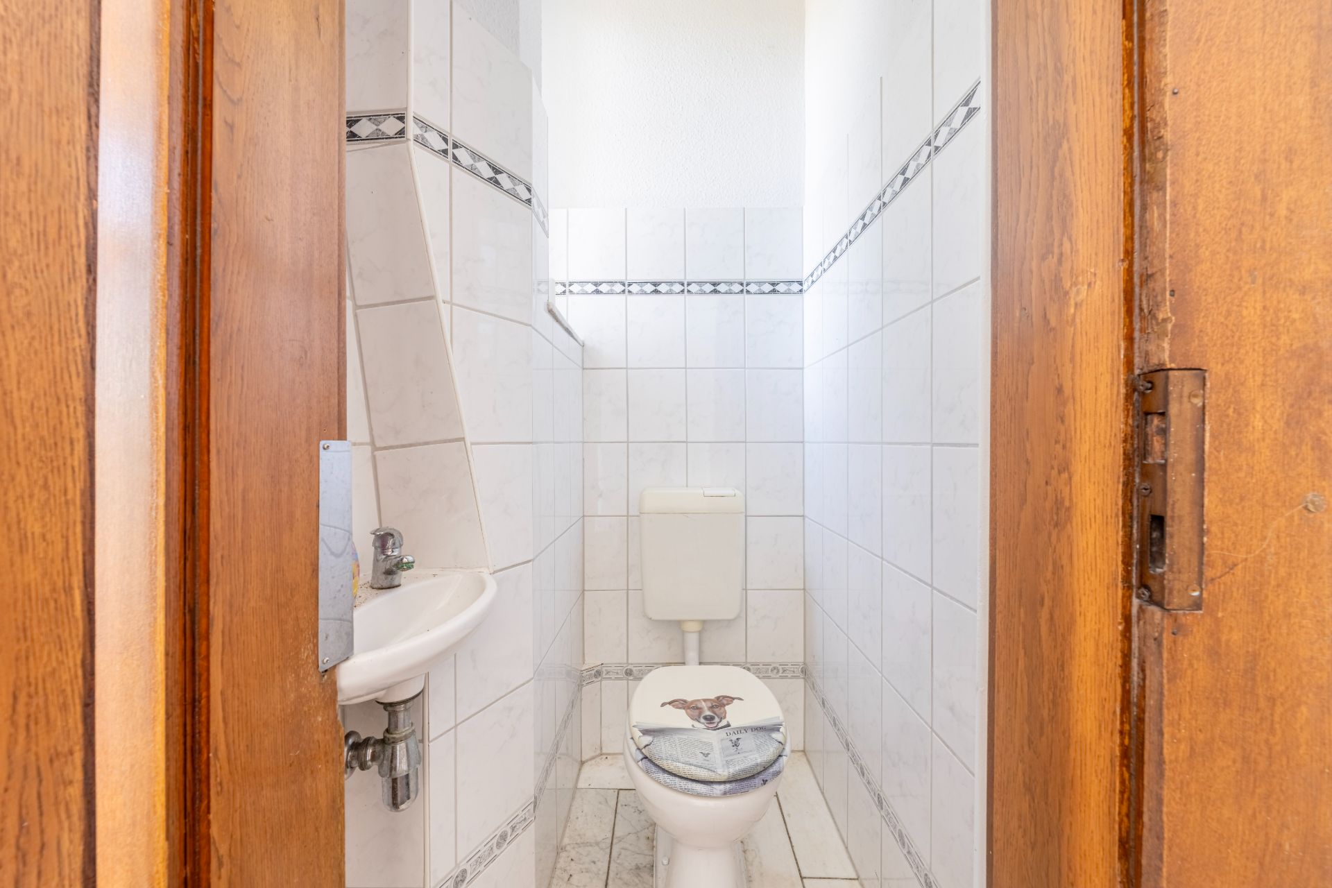 Kleines Badezimmer mit weiß gefliesten Wänden, Toilette und kleinem Waschbecken.