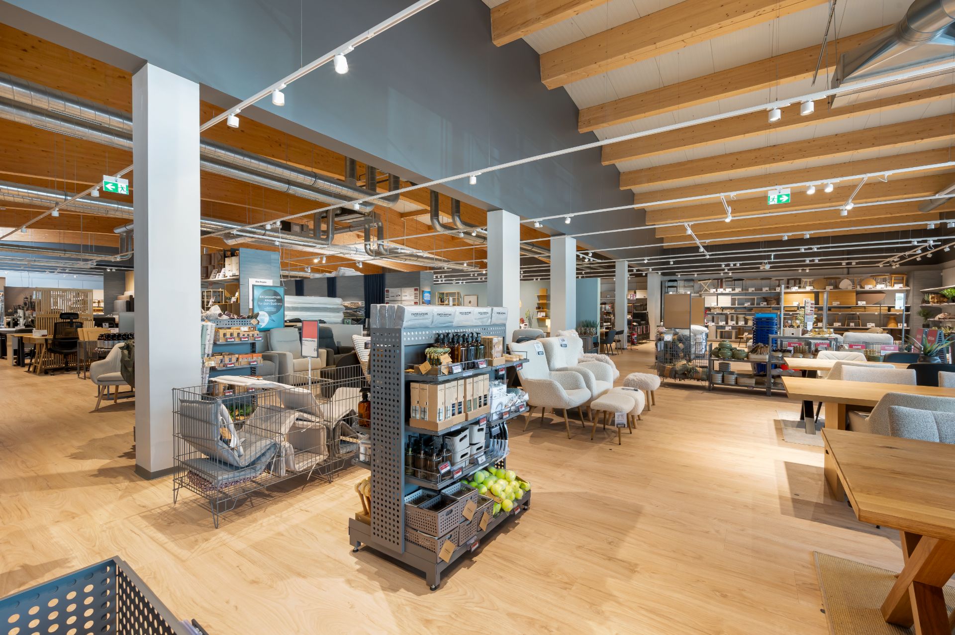 Großer, moderner Raum mit Holzdecke, mehreren Sofas, Sesseln und Regalen mit Produkten.
