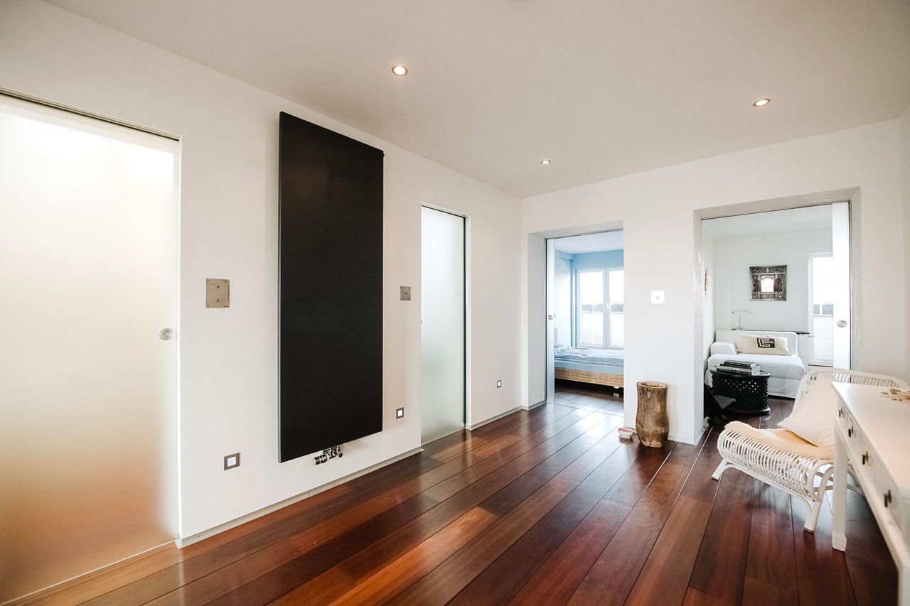 Heller Flur mit Holzboden, zwei offenen Türen zu Wohnzimmer und Schlafzimmer, moderner Einrichtung.