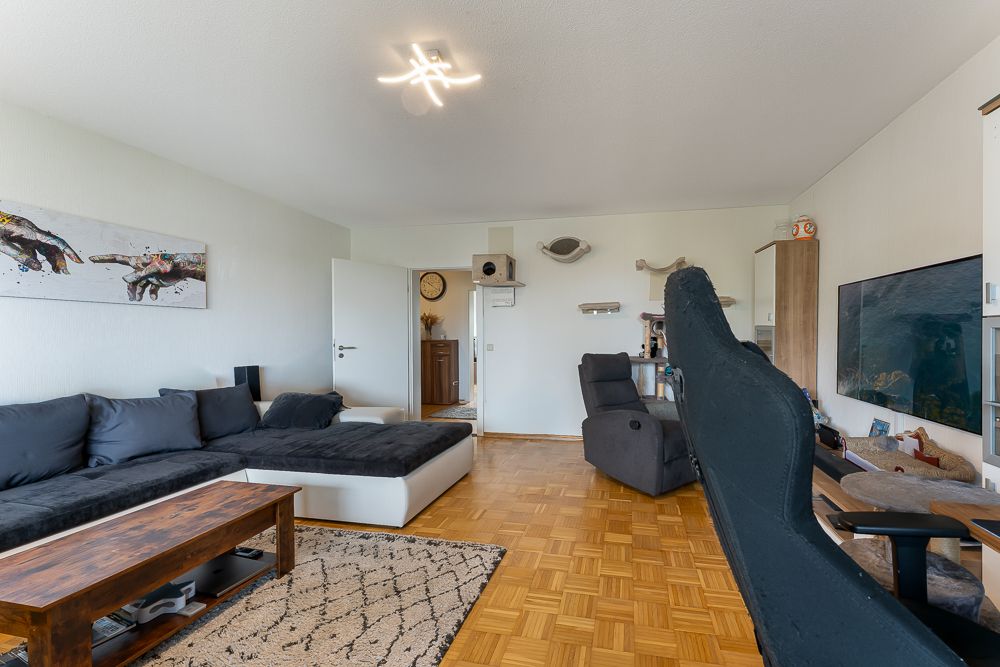 Wohnzimmer mit großem Sofa, Holz-Couchtisch, Sessel, Teppich und Fernseher an der Wand.