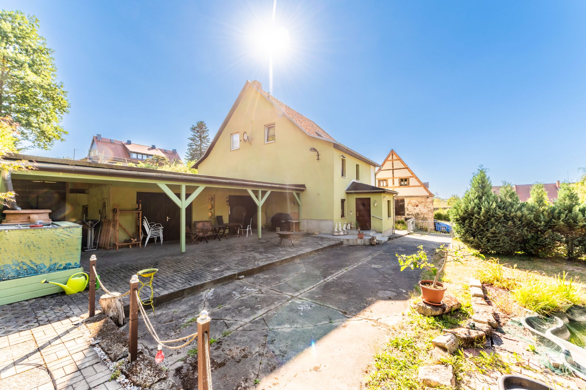 Haus mit gelber Fassade, Carport, Hofbereich und Garten mit Sonnenschein.
