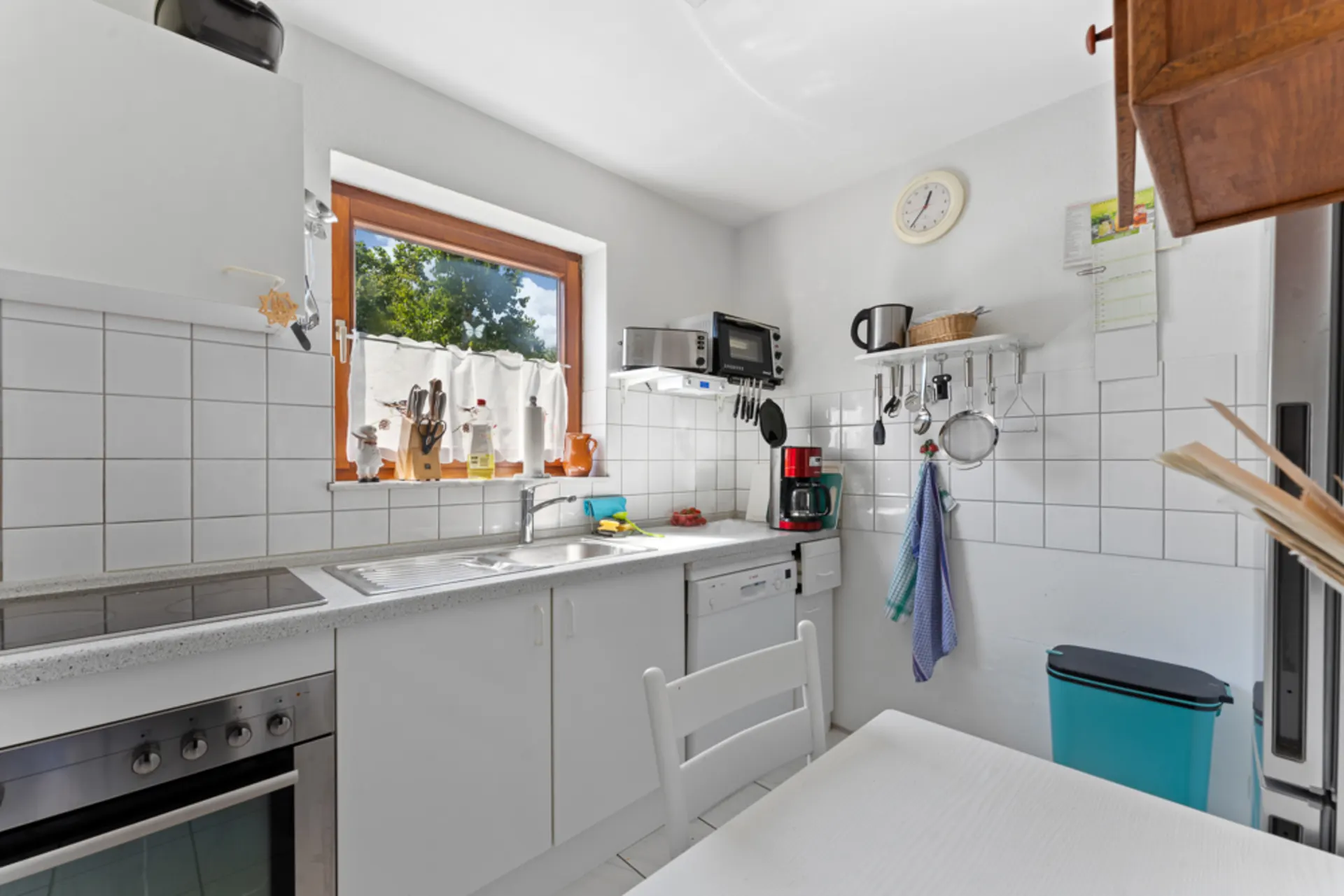 Helle Küche mit weißen Schränken, großem Fenster, Spüle und verschiedenen Küchengeräten.