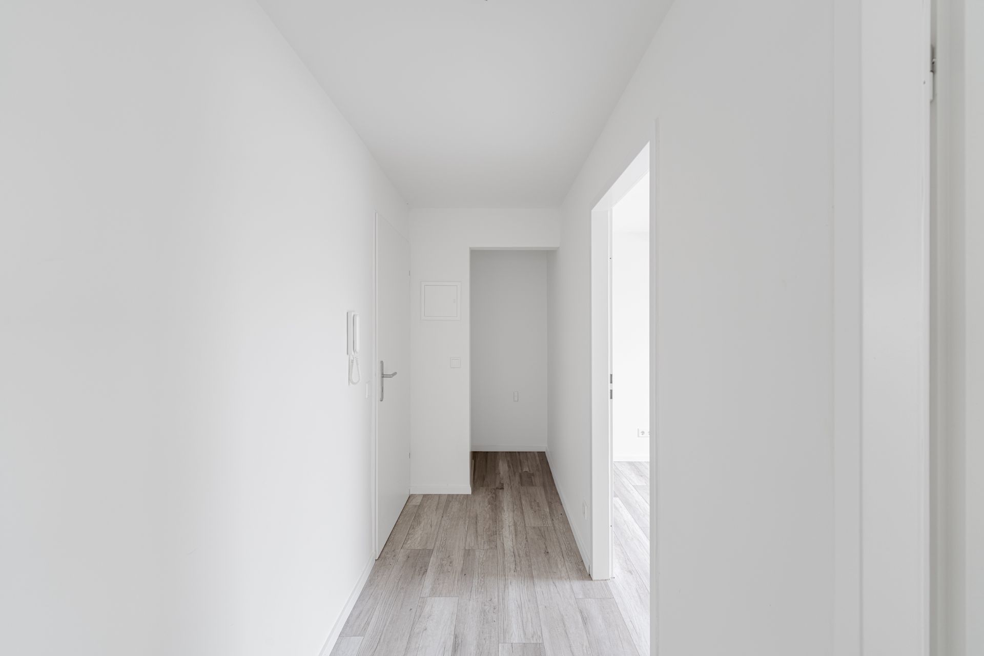 Heller Flur mit weißen Wänden und hellgrauem Holzboden in einer Wohnung.