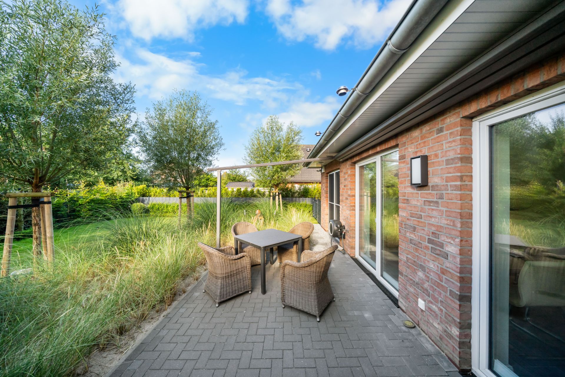 Terrasse mit Tisch, vier Stühlen und Blick auf einen Garten neben einem Backsteinhaus.
