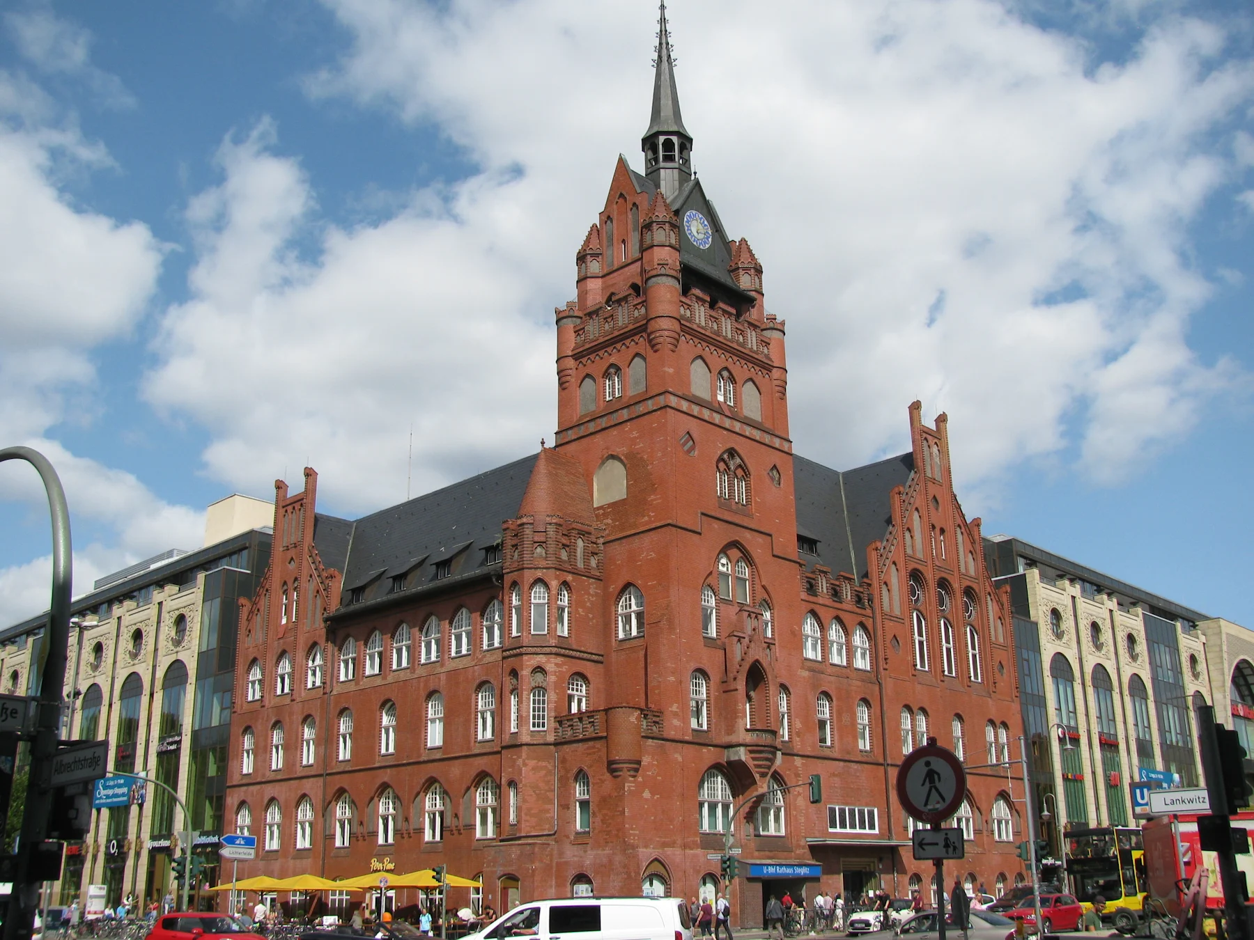 Großes rotes Backsteingebäude mit Turm und Uhr an einer belebten Straßenecke.