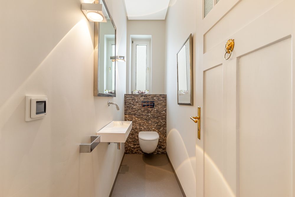 Modernes kleines Bad mit Wand-WC, Waschbecken, Spiegel und Fenster am Ende des Raums.