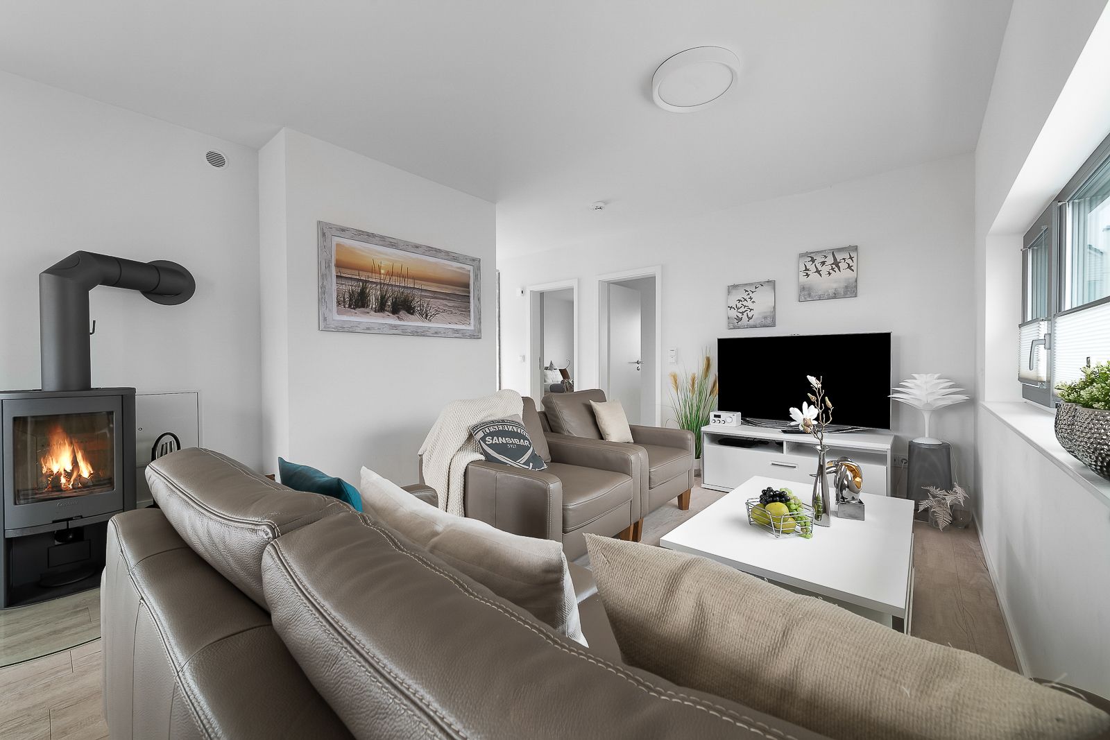 Modernes Wohnzimmer mit Ledersofa, Kaminofen, Fernseher und großem Fenster.