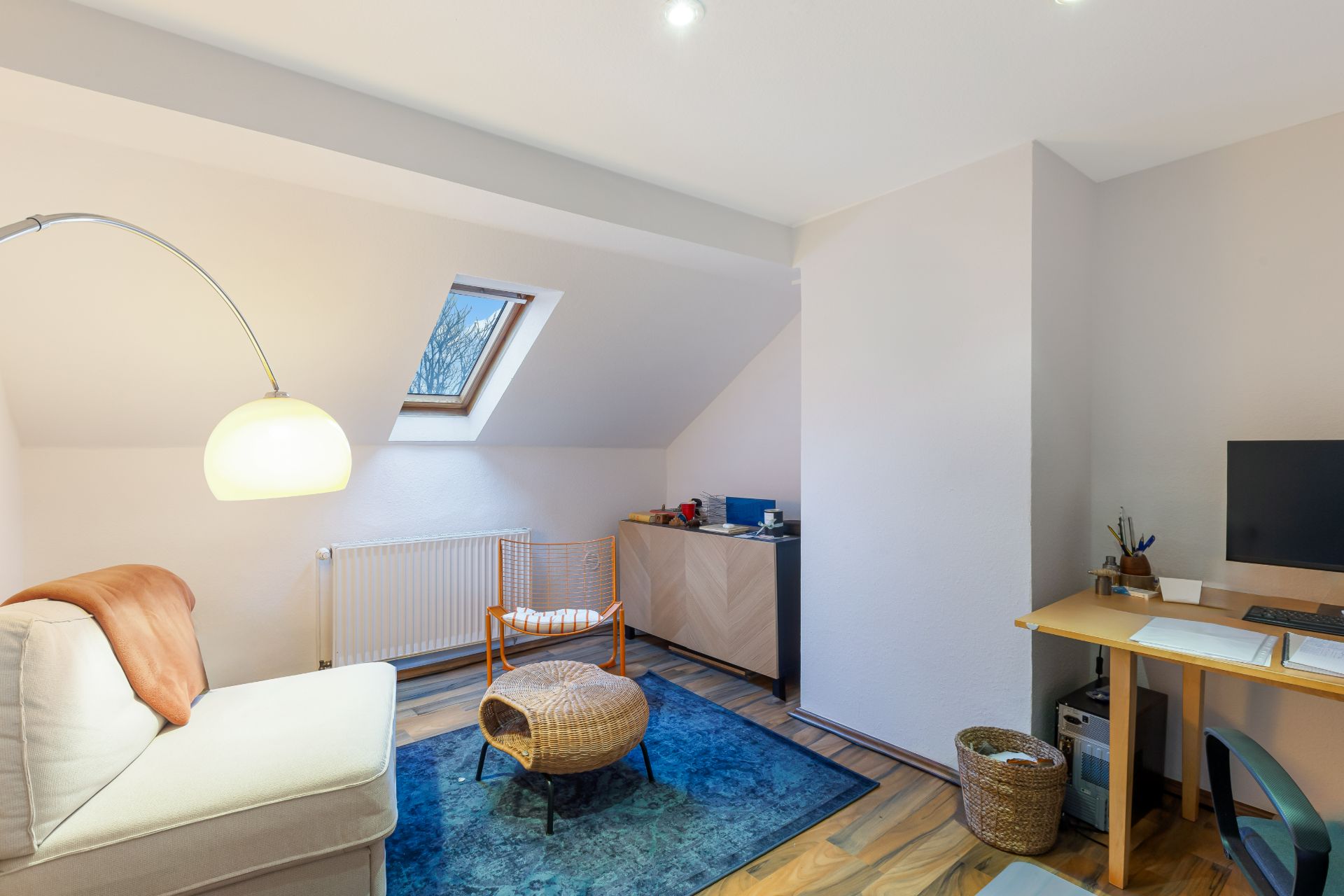 Helles Arbeitszimmer mit Sofa, Schreibtisch, Stuhl, Teppich, Sessel und Dachfenster.