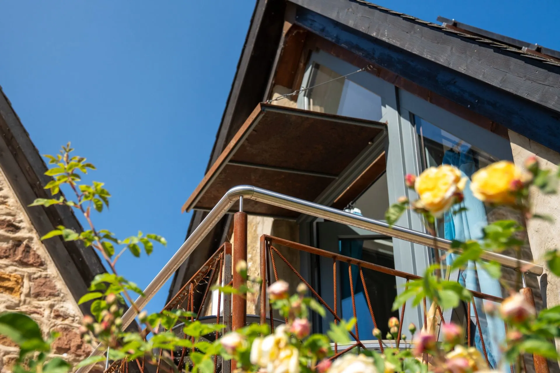 Balkon eines Hauses mit Blumen im Vordergrund und blauem Himmel.
