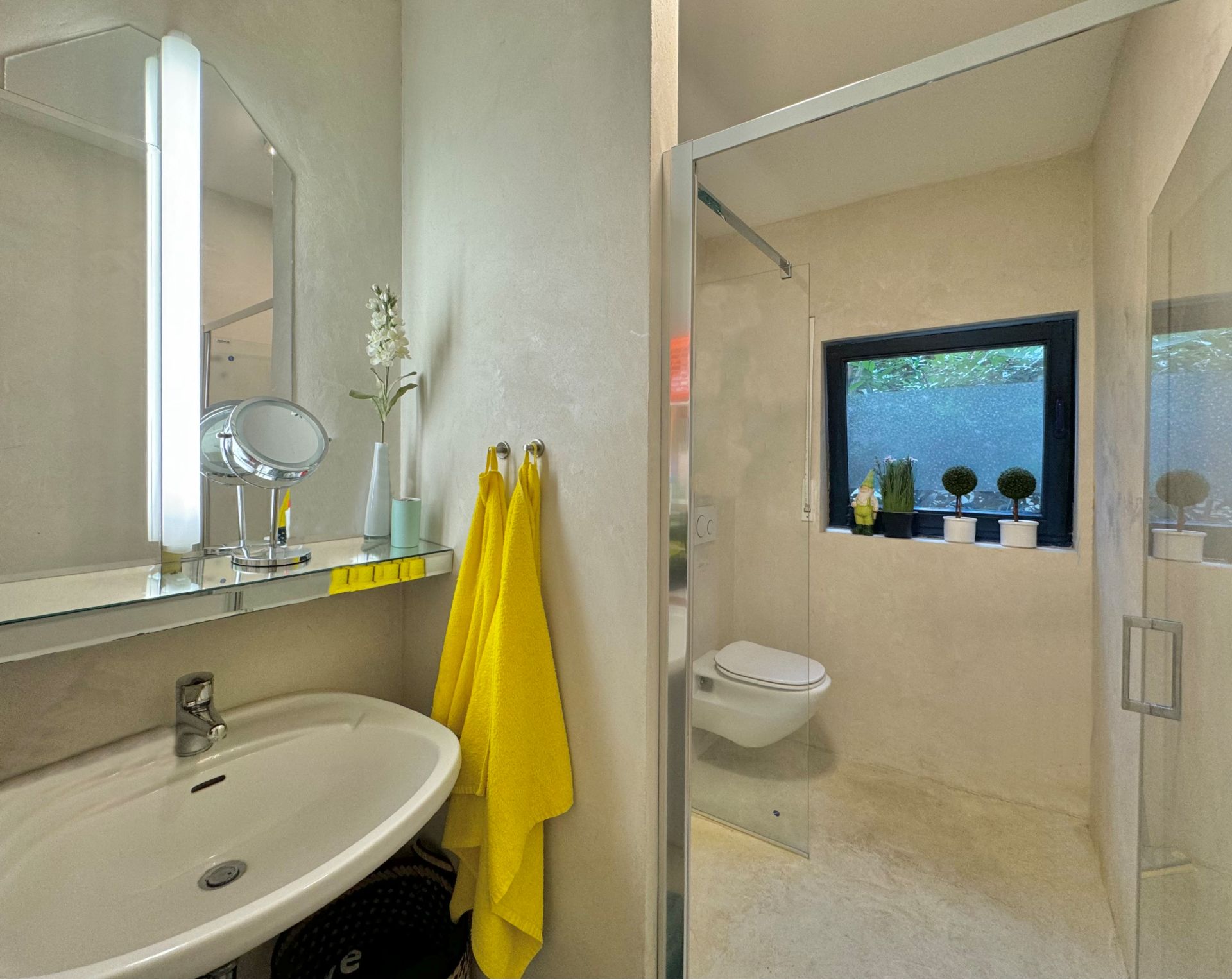 Modernes Badezimmer mit Waschbecken, Spiegel, gelben Handtüchern und ebenerdiger Dusche.