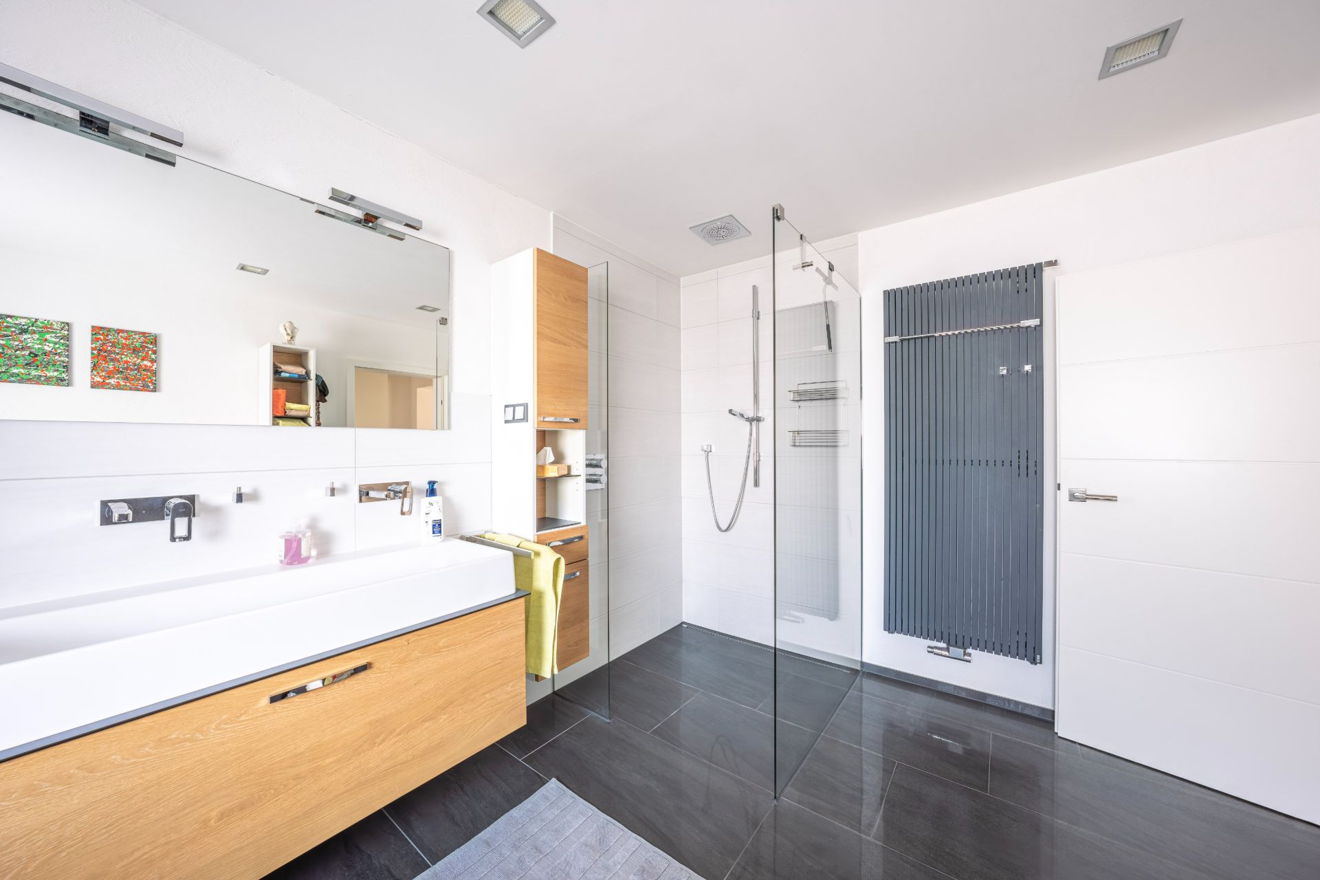 Modernes Bad mit großer Dusche, Waschbecken, Spiegel und Handtuchheizkörper.