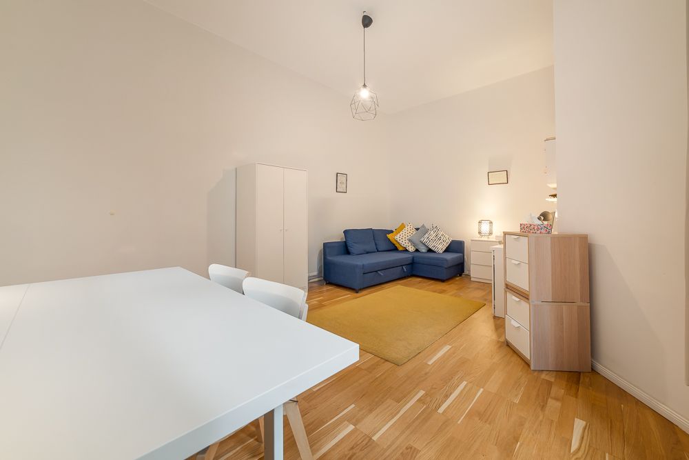 Helles Wohnzimmer mit blauem Sofa, gelbem Teppich, weißem Tisch und Schrank auf Holzboden.