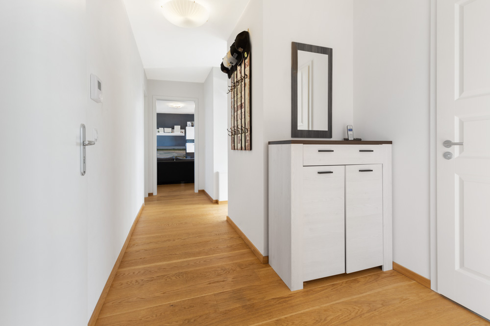 Heller Flur mit Holzfußboden, Kommode, Spiegel und Garderobe an der Wand.