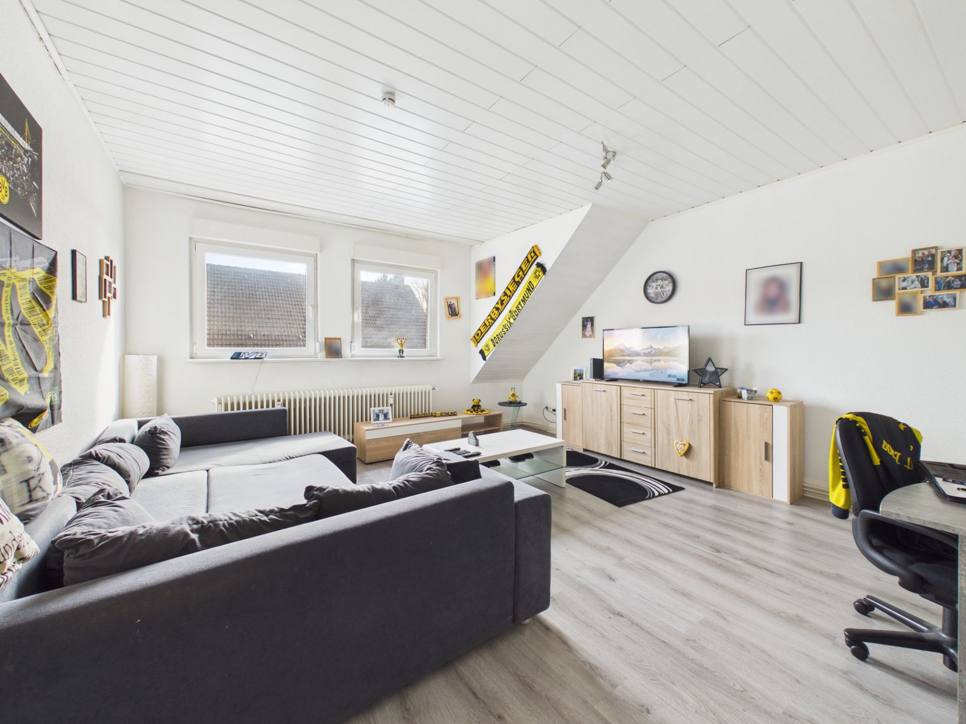 Helles Wohnzimmer mit grauem Sofa, Couchtisch, TV und Schreibtisch auf hellem Holzboden.