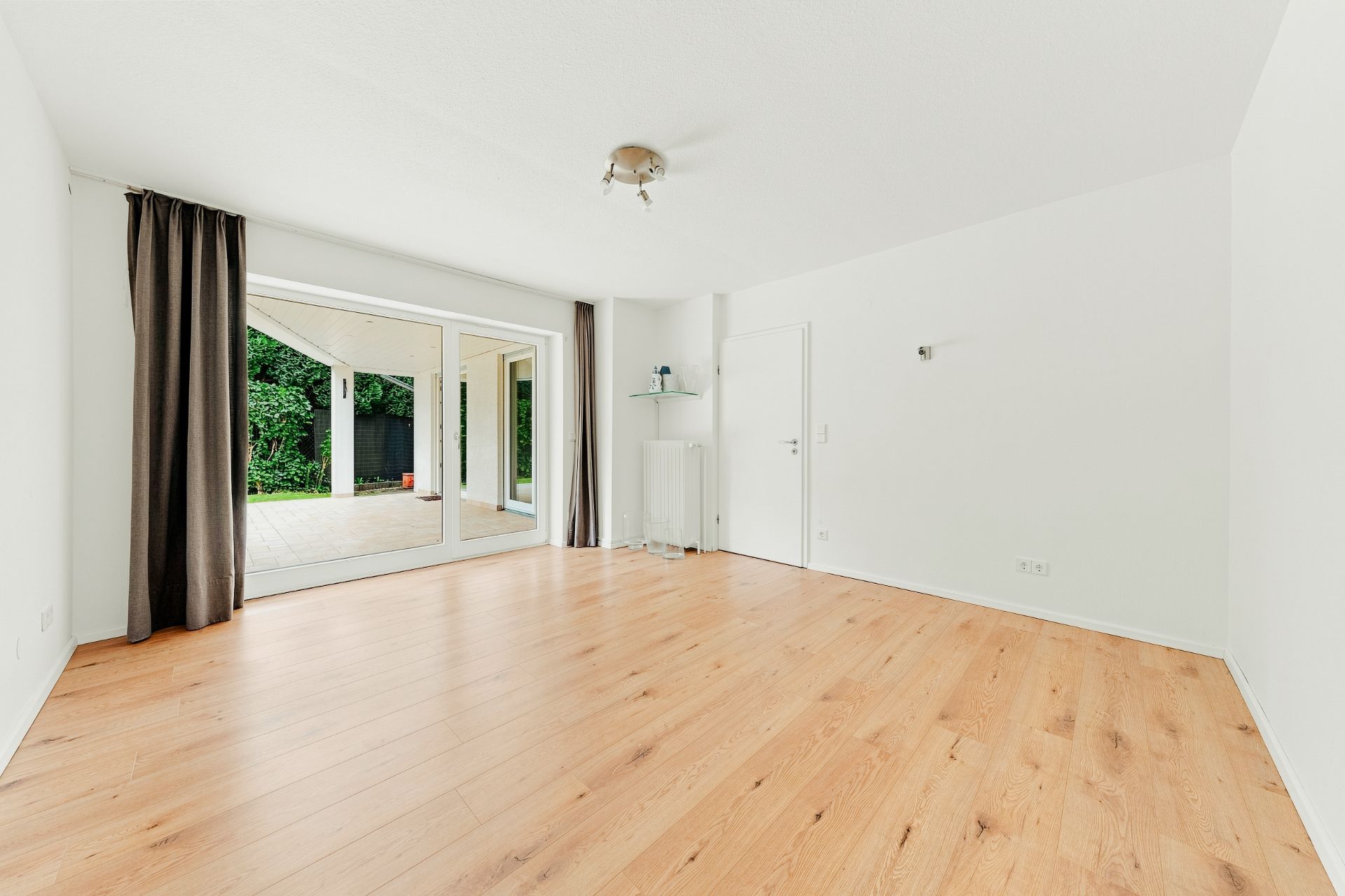 Helles Wohnzimmer mit Holzfußboden, großen Fenstern und Zugang zur Terrasse.